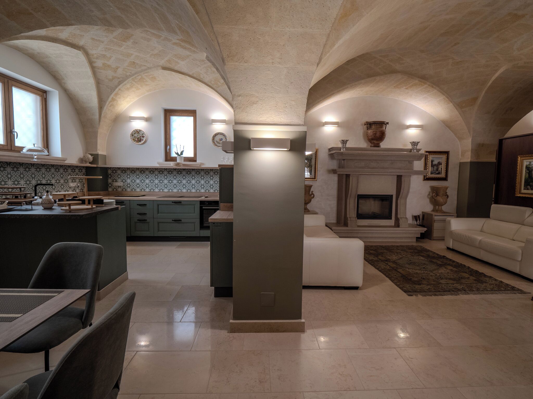 Uma sala de estar ampla com lareira, uma área de jantar com cozinha ao fundo e um teto alto e arqueado.