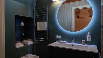 Une salle de bain avec un miroir rond, un bidet, des toilettes et un lavabo.