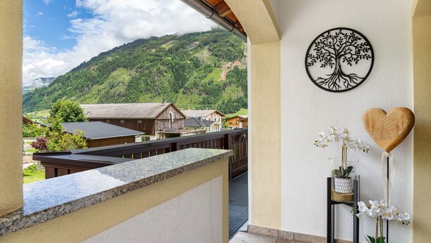 Een balkon met uitzicht op een bergachtig landschap, een boomdecoratie aan de muur en een hartvormig object.