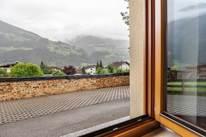 A view from a window overlooking a paved area with a stone wall and a metal grate, with houses and mountains in the background. - Apartment Eva – Cozy Retreat in the Heart of Zillertal (Ried im Zillertal)