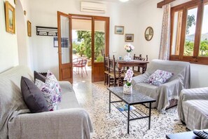 Ein Wohnzimmer mit einer Couch, Sesseln, einem Couchtisch und einem Essbereich mit Stühlen und Tisch.