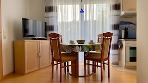 Een eetgedeelte met een televisie, houten kasten, een tafel met stoelen en een keuken met een oven.