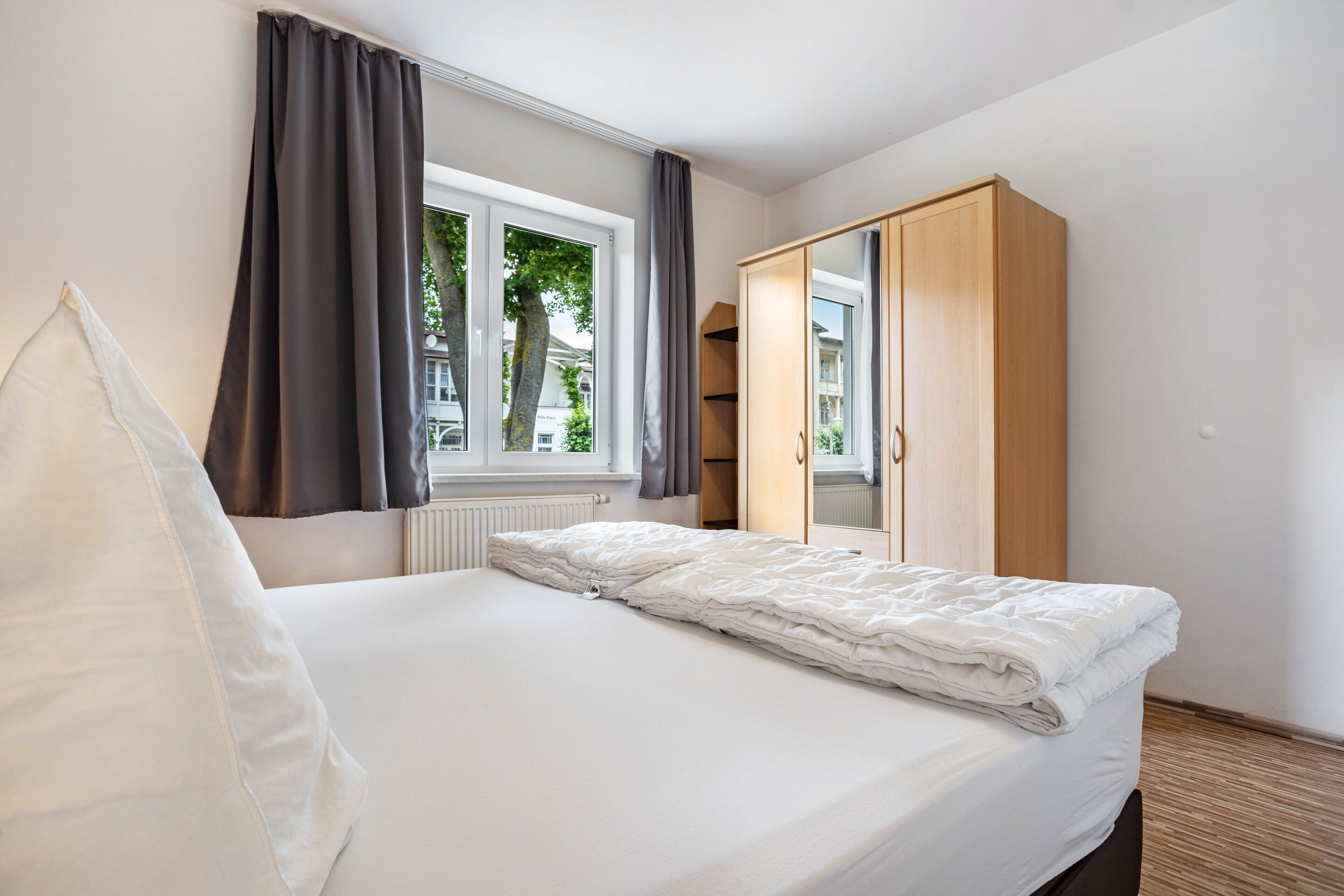 Ein Schlafzimmer mit Bett, Kleiderschrank, Fenster und Heizkörper.