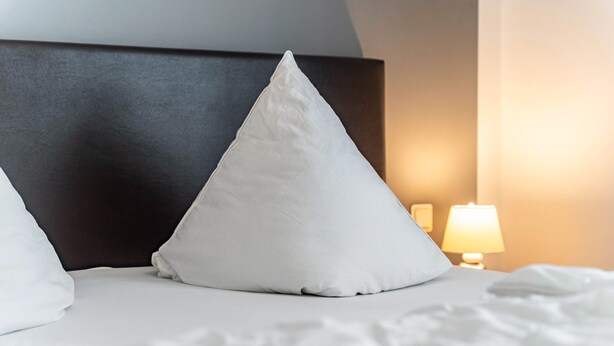 Un lit bien fait, avec une literie et des oreillers blancs, une tête de lit sombre et une lampe de chevet.