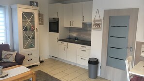 Eine kleine Küche mit weißen Schränken, einer Mikrowelle, einem Spülbecken und einem Mülleimer.
