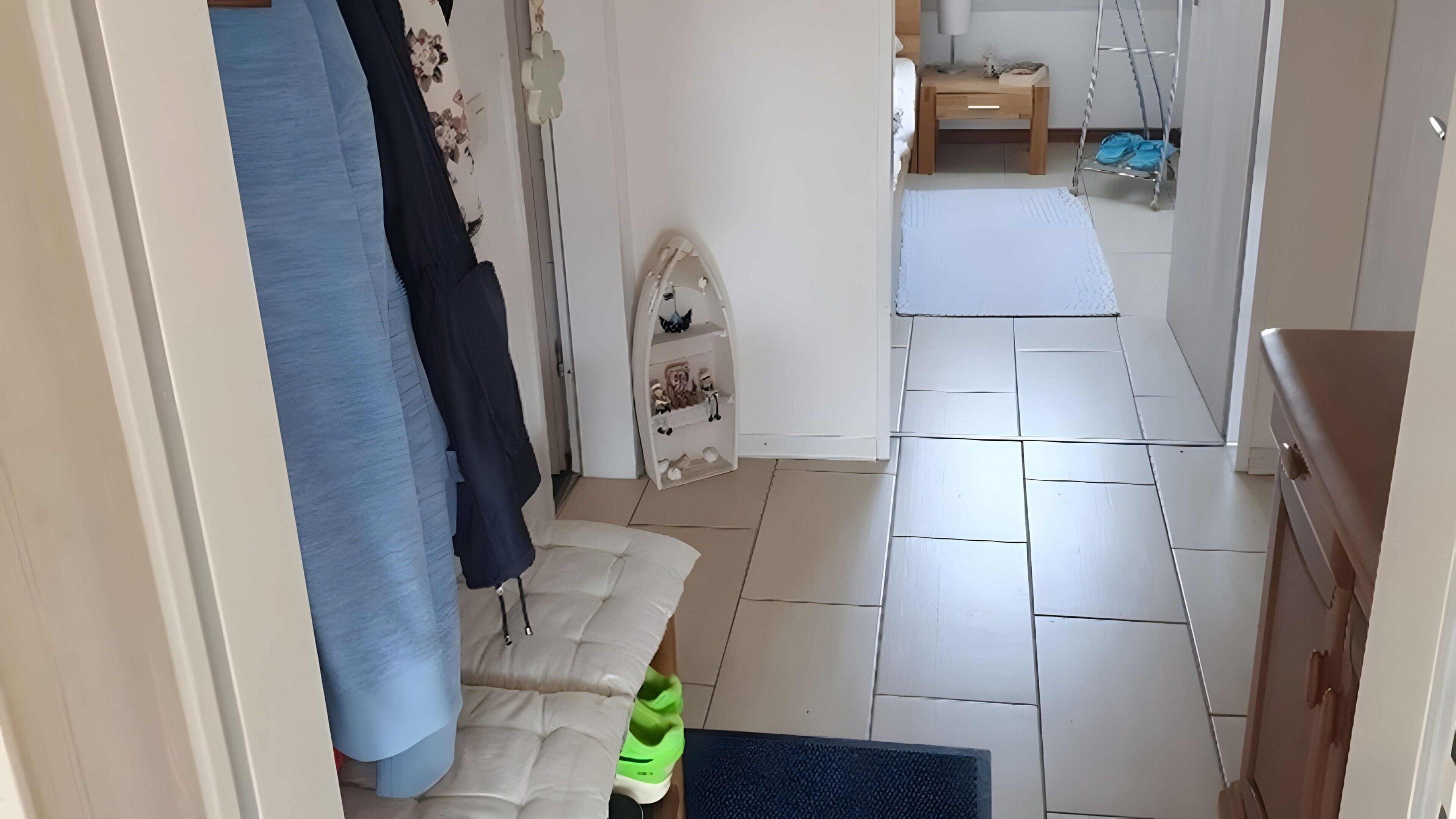 A narrow hallway with a bed, a small table, a chair, and a hanging shoe rack.