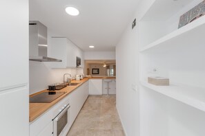 Uma cozinha moderna com armários brancos, bancada de madeira e forno embutido.