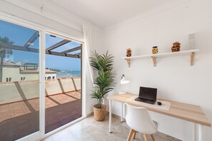 Ein Balkon mit Blick auf das Meer, ein Schreibtisch mit einem Laptop, eine Topfpflanze und Dekorationselemente auf Regalen.