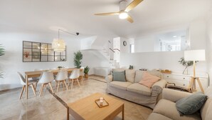 Een moderne woonkamer met een bank, salontafel, eettafel, stoelen en een plafondventilator.
