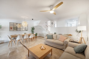 A modern living room with a sofa, coffee table, dining table, chairs, and a ceiling fan.