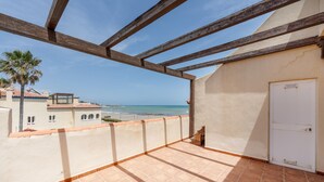 Een balkon met uitzicht op het strand, houten balken en een witte deur.