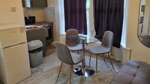 Une cuisine compacte équipée d’un réfrigérateur, d’un four et d’un four à micro-ondes. On y trouve une table à manger avec quatre chaises, ainsi qu’un canapé dans l’espace salon.