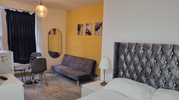 Une chambre d’hôtel comprenant un lit, un canapé, un bureau avec des chaises, un miroir et des œuvres d’art accrochées au mur.
