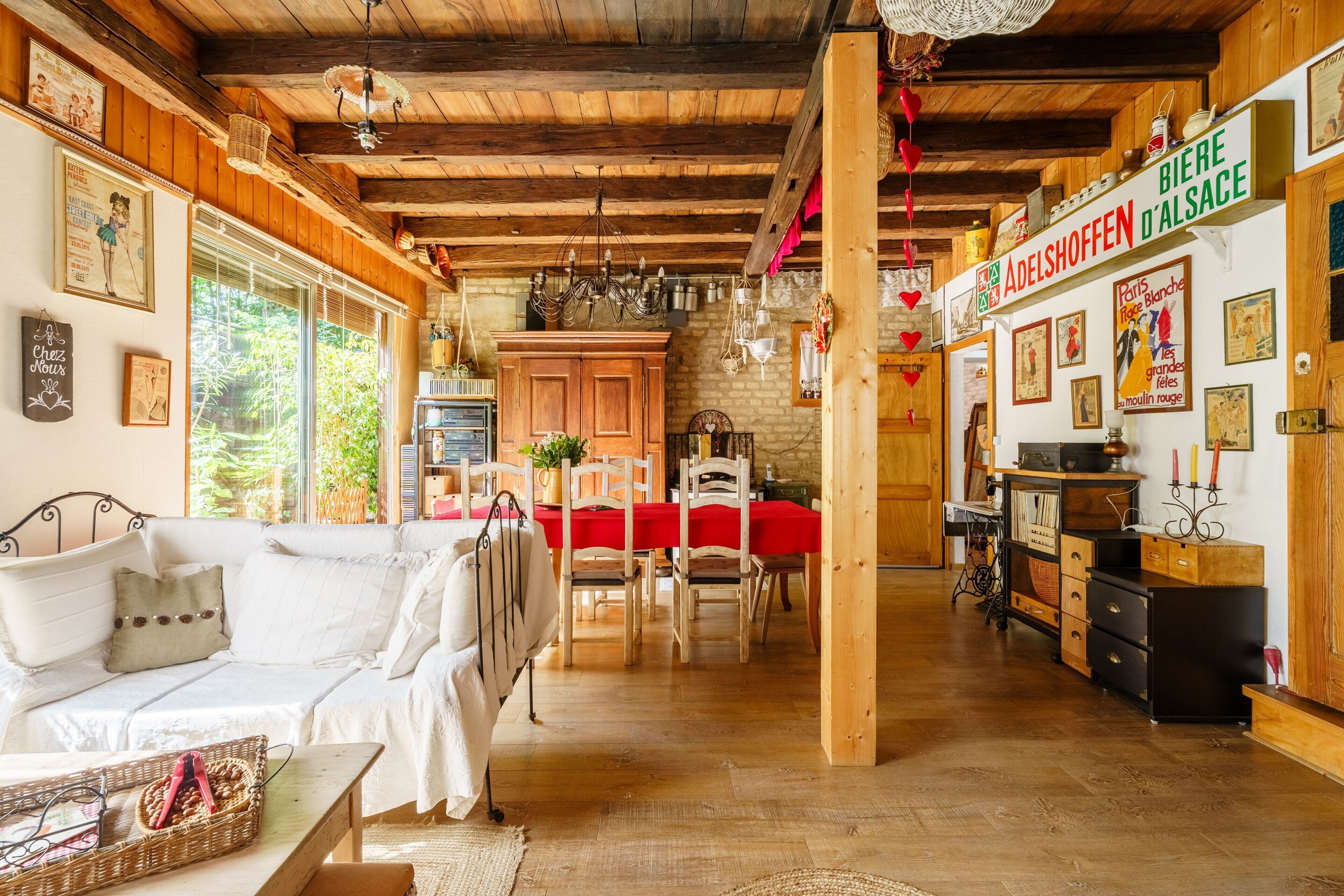 Ein gemütlicher Innenraum mit Holzboden, einem Essbereich mit roter Tischdecke und einer Küche mit Holzschränken sowie einem Schild mit der Aufschrift 'BIERE D'ALSACE'.