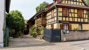 A traditional half-timbered building with a gated entrance, a visible staircase, and a sign indicating 'La Cour de J'Anne.' - Gite Geranium – La Cour de J'Anne in the Heart of Old Schiltigheim (Schiltigheim)