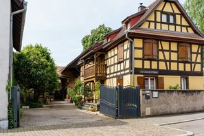 Ein traditionelles Fachwerkhäuschen mit geschlossenem Eingang, einer sichtbaren Treppe und einem Schild mit der Aufschrift 'La Cour de J'Anne'.