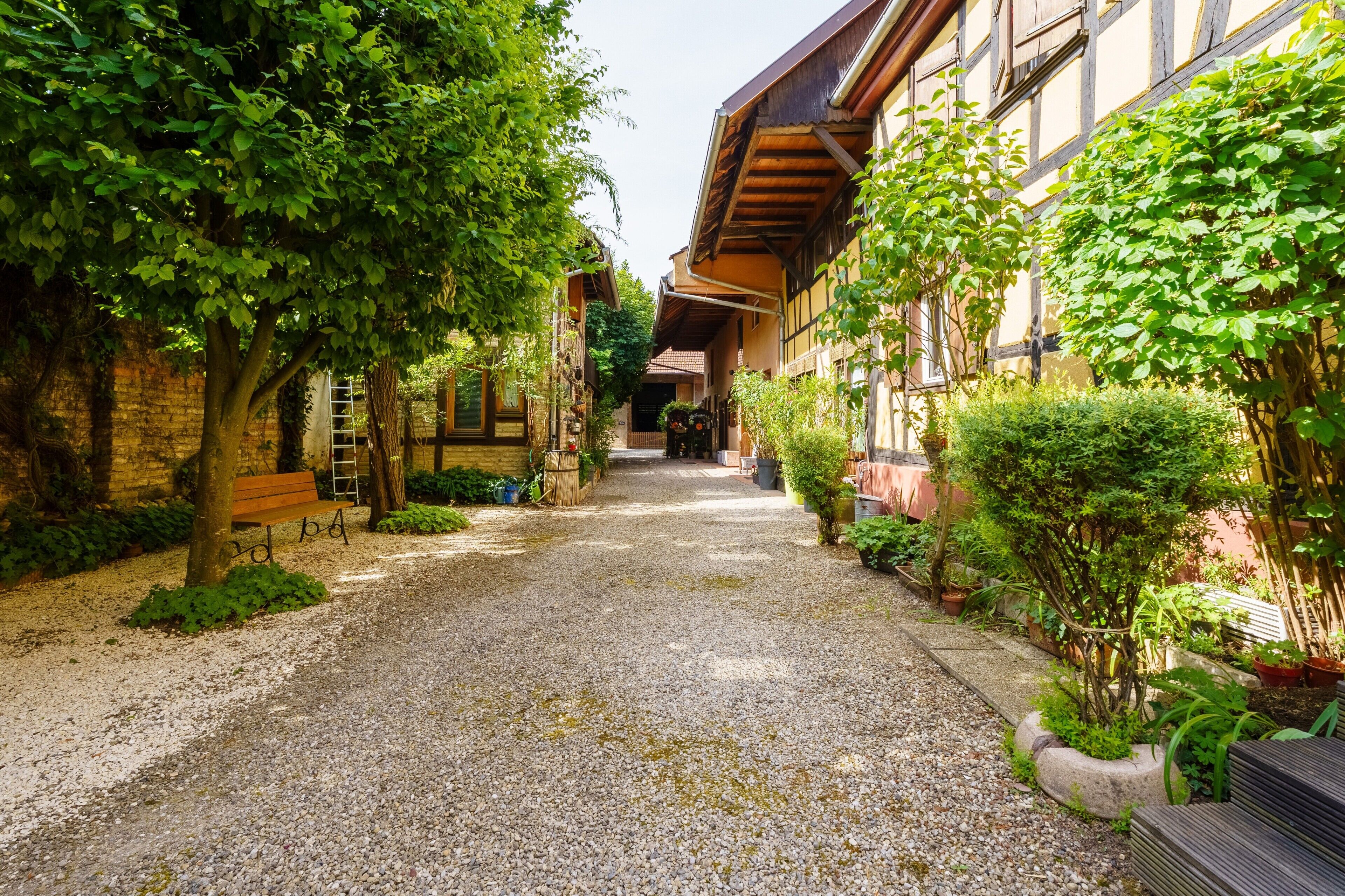 A narrow gravel path flanked by buildings with wooden facades and greenery.