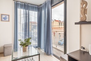 Una habitación con una mesa de vidrio, una planta en maceta, un sofá, un ventanal con cortinas azules y una decoración con forma de caballito de mar.
