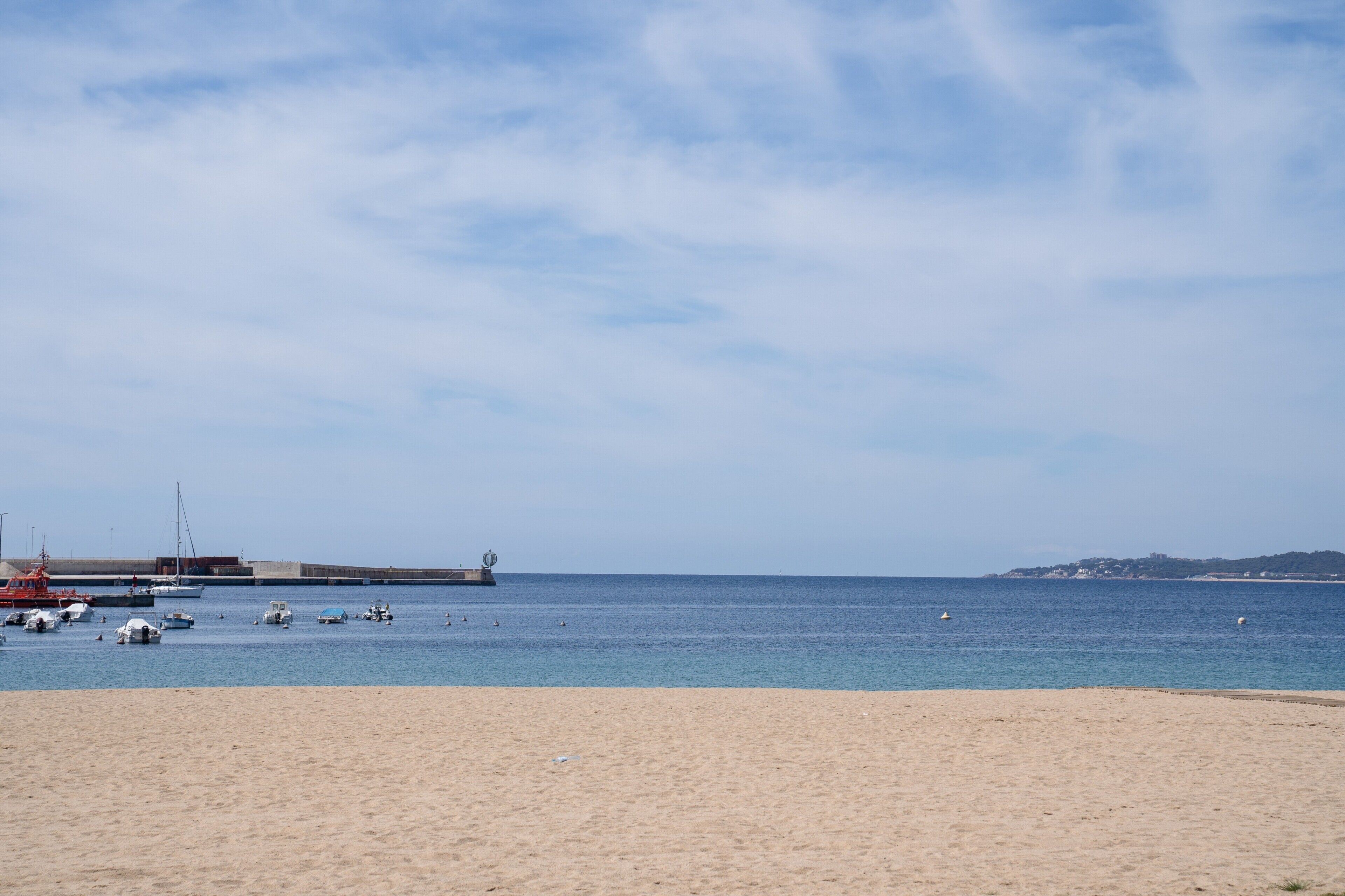 A beach with boats, a pier, and a distant hill.