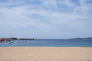 Una playa con barcos, un muelle y una colina distante.