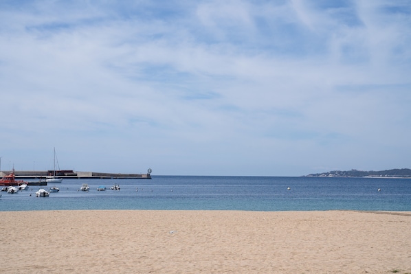 Une plage avec des bateaux, une jetée et une colline qui se dessine à l’horizon.