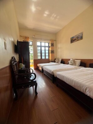 Une chambre d’hôtel avec deux lits, un banc en bois, une télévision et une fenêtre avec des rideaux.