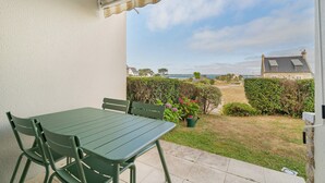 Eine Terrasse mit Tisch und Stühlen, Blick auf das Meer und ein Hecke im Hintergrund.