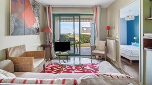 Ein Zimmer mit einer Couch, einem Sessel, einem Fernseher, einem Tisch und Blick durch eine Glastür.