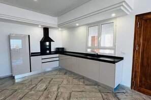 Una cocina con extractor de aire negro, armarios blancos, encimera negra y una ventana con persianas.