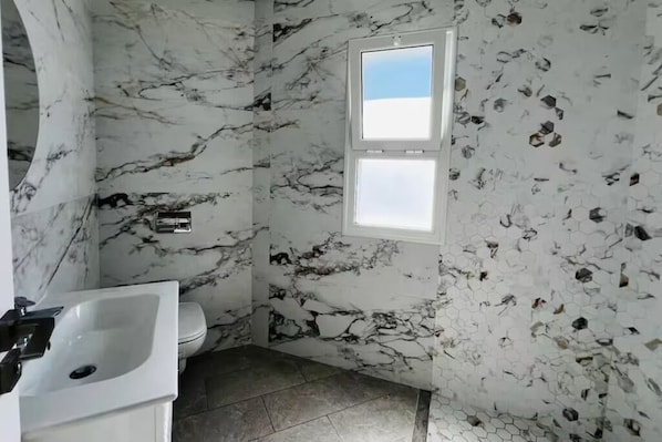 Un baño con pared de mármol, un lavamanos y un inodoro.