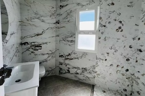 Un baño con pared de mármol, un lavamanos y un inodoro.