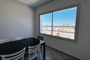 Una habitación con un ventanal grande, una mesa negra, sillas blancas y vista a la playa.