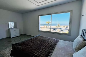 Un dormitorio con cama, cómoda, ventana con vista a la playa y al estacionamiento.
