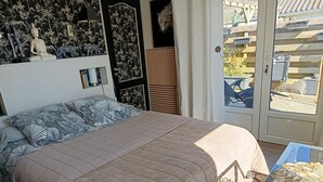 A bedroom with a bed, a nightstand, a window with a view of the outside, and a door. - Guest Room “La Coccinelle Des Cap - Taupe Zen” with Sea View, Private Terrace & Wi-Fi (Ambleteuse)