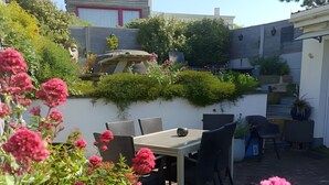A patio with a table and chairs, surrounded by lush greenery and pink flowers. - Guest Room “La Coccinelle Des Cap - Taupe Zen” with Sea View, Private Terrace & Wi-Fi (Ambleteuse)