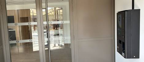 A hotel entrance with a glass door, a patterned rug, and a wall-mounted device.