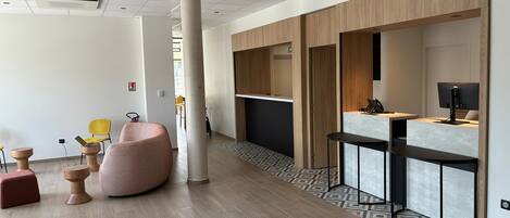 A modern hotel lobby with a reception desk, seating area, and a large pillar.