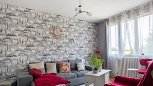 A living room with a grey sofa, red chair, white table, and a patterned wall.