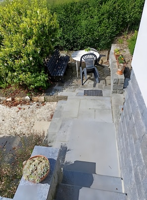 Een terras met een tafel en stoelen, een plant in een pot en een stenen muur.