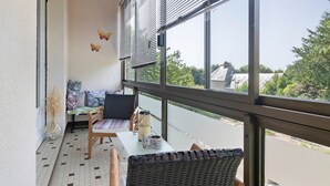 A balcony with a table, chairs, a vase, and a view of greenery.