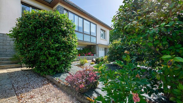 A house with a well-maintained garden, a stone pathway, and a large window.