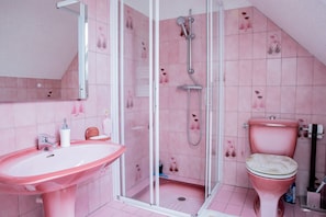 A bathroom with pink tiles, a glass shower enclosure, a pink sink, and a toilet.