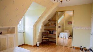 Un dormitorio con techo inclinado, una silla de madera, una cama, una estantería y un espejo.