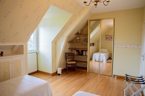 A bedroom with a sloped ceiling, a wooden chair, a bed, a bookshelf, and a mirror.