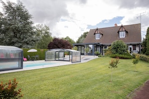 A house with a swimming pool, a covered patio, and a well-maintained lawn.