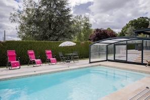 A swimming pool with lounge chairs and a covered seating area.