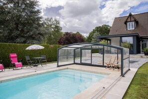 A swimming pool with a glass enclosure, pink chairs, and a house in the background.