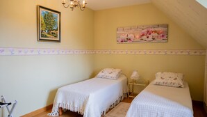 A bedroom with two beds, a chandelier, a painting, and a decorative border.
