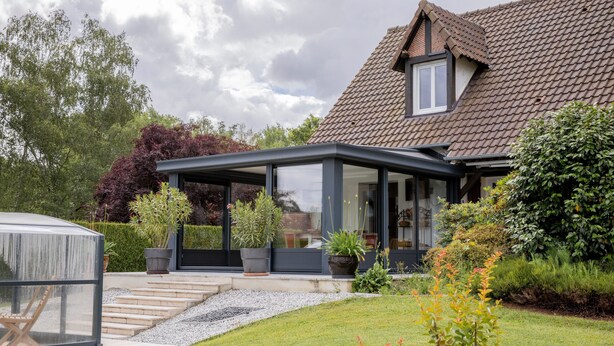 A house with a conservatory, a garden with various plants, and a clear sky.