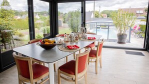 A conservatory with a dining table, chairs, and a view of a swimming pool and garden.